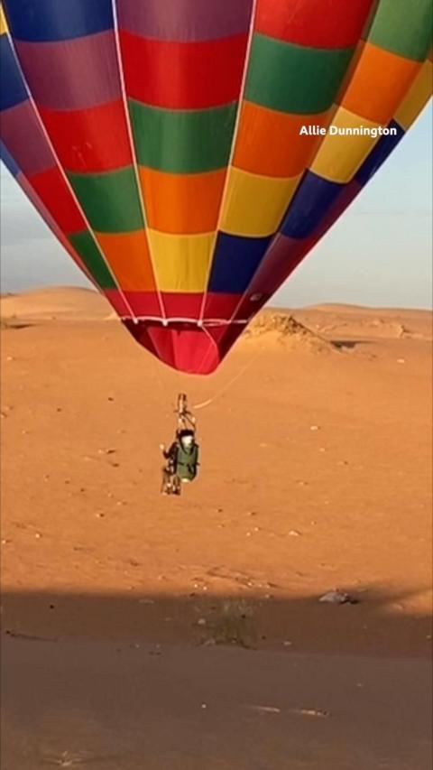 Allie Dunnington lands a rainbow coloured balloon on a sandy landscape beneath her.