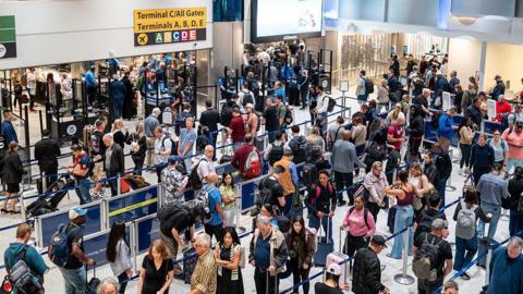 long line of people with suitcases waiting for a security checkpoint in airport