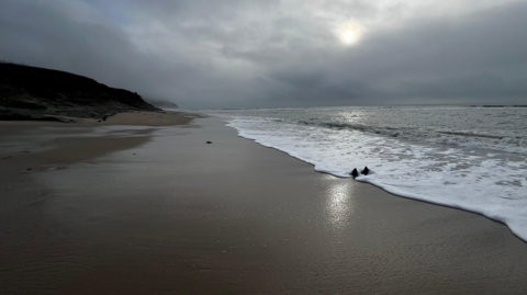 A sandy beach with a low sun pushing through the cloud