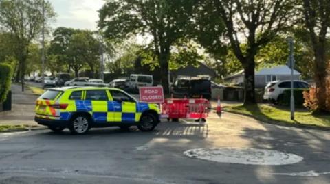 A police car sits ahead of a road closed sign on the road