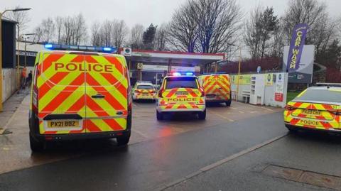 Five police vehicle at the scene at Gilwilly Industrial Estate in Penrith. There is a "car wash" sign next to where the vehicles are parked.