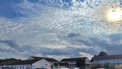 Sun peeking through speckled cloud above a row of houses 