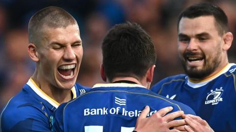 Sam Prendergast (left) and Max Deegan (right) congratulate Jimmy O'Brien after he scored one of Leinster's five tries