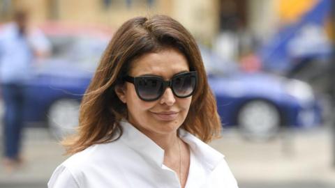 Zamira Hajiyeva, who is smirking at the camera, is wearing a white shirt and sunglasses. She has brown, shoulder length hair 