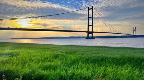 The Humber Bridge lit by the Sun breaking through cloud