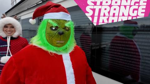 A Grinch in a Santa costume and the Strange logo