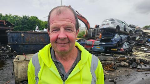 Ray Kirk stands in front of tower of cars