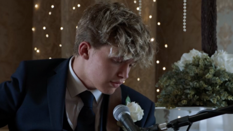 A screenshot of the Gavin and Stacey finale of Oscar Hartland, who plays Neil the baby, is wearing a suit and is singing into a microphone. 
