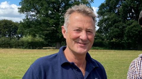 Anthony Froggatt wearing a blue polo-shirt smiles at the camera in a field