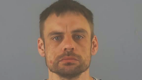 Police custody photo of Tom Ellison who has short, dark hair and a beard.