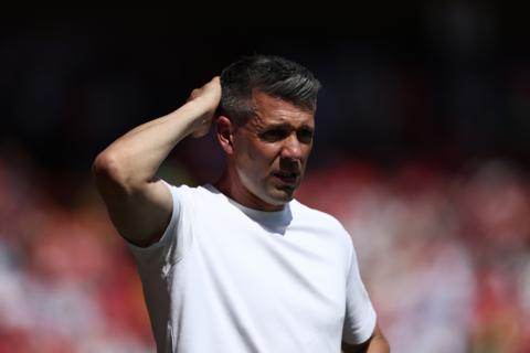 Paulo Pezzolano, wearing a white t-shirt, scratches the back of his head.