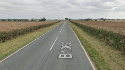 A Google street view of the B1362. The two-lane road is clear with no vehicles and there are grass verges and fields either side of the road.