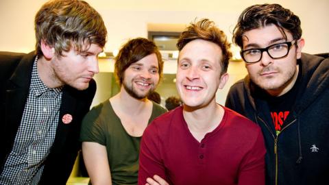 Members of The Futureheads in a row from left to right wearing a checked shirt and a black jacket, a green T-shirt, a red top and a black hoodie