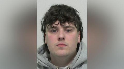 Mugshot of Frier. He is clean shaven with long straggly dark hair. He has a nose ring in his left nostril and is wearing a grey hoody.
