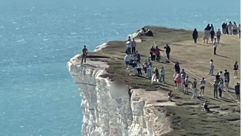 Dozens of people photographed from a distance dangerously close to the edge of chalk cliffs at Beachy Head in East Sussex.