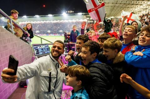 Young fans pose for a selfie as England Under-21s play at Ashton Gate. They are all smiling as a man holds a camera for the picture with the interior of the stadium visible in the background