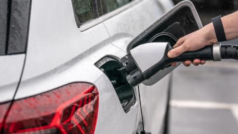 A hand plugging a charger into an electric car