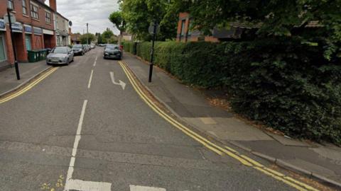 Generic image of Villa Road, with cars on both sides of the street. There are trees and bushes to the right of the road on the photo, approaching the junction in the foreground.