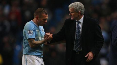 Craig Bellamy shakes hands with a suited Mark Hughes after a Manchester City game