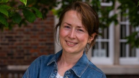 Fiona Packe wearing a blue denim jacket and small earrings, smiles at the camera