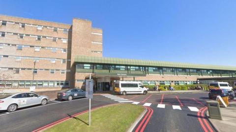 An external view of the Freeman Hospital in Newcastle. Taxis and patient transport buses wait outside.