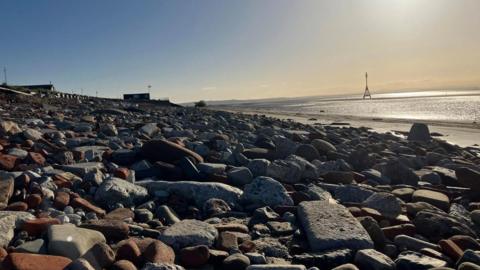 A view over 'Blitz Beach' showing piles of stone, bricks and ceramic on a beach at sunset