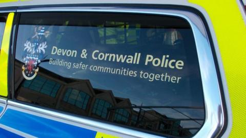 The window of a police vehicle which has a 'Devon & Cornwall Police Building safer communities together' sticker on it with the logo to the left.