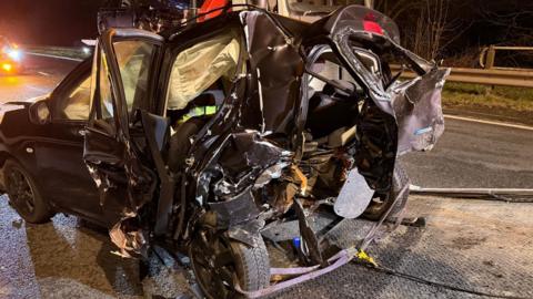 A close up of a black car that is completely crumpled