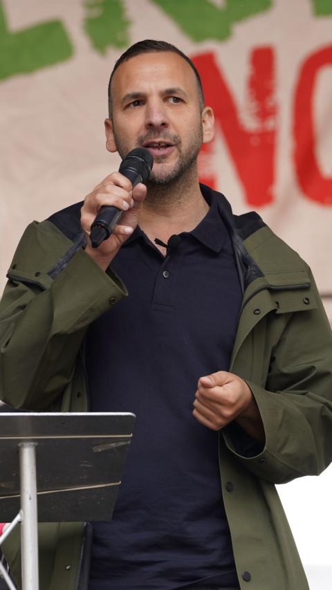 Zack Polanski, Green Party leader, wearing a navy top and a green jacket speaking into a microphone