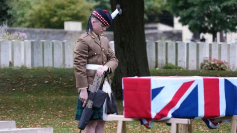 Soldier standing next to a coffin draped in the Union Jack