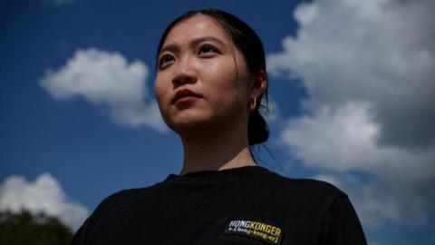 Anna Kwok photographed from below, hair tied into a bun, wearing a black t-shirt reading HONGKONGER