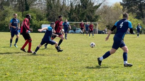 Two opposing football teams playing on the downs. One is going for the ball. It is a sunny day. 