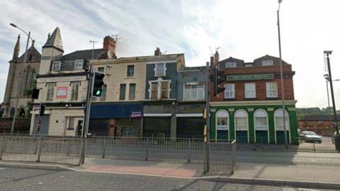 A row of buildings includes The Throstles Nest pub on the left, what looks like housing in between and The Eagle Vaults on the right hand side.