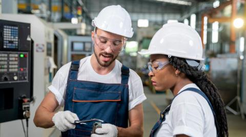 Two engineers wearing white hard hats looking at a piece of machinery