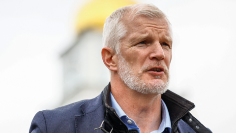 British Minister of State for Armed Forces Al Carns speaks during an interview He has short grey hair and a trimmed grey beard, wearing a blue collared shirt under a dark jacket and a padded outer layer. 