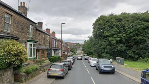 A view of a residential street lined with terraced houses and cars. At the bottom of the street is a Lidl.