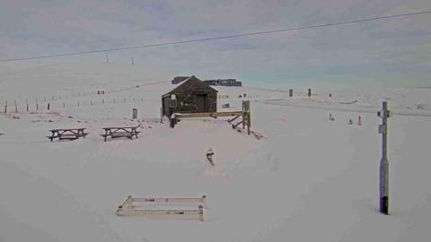 An area covered in snow, there are two benches, a hut and a lamppost. 