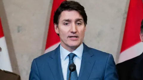 Justin Trudeau stood at a podium in a suit and tie and microphone infront of him