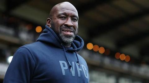 Darren Moore stands in his navy blue hoodie with the the letters PVFC on the front watching on from the touchline