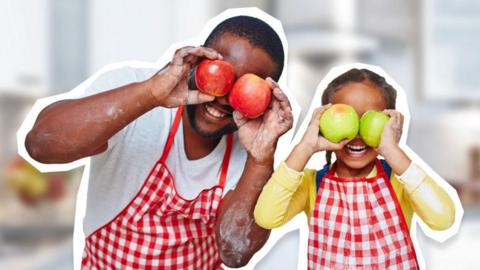 An adult and child smiling while holding apples in front of their eyes