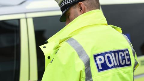 A man wearing a police jacket while standing by a police car.