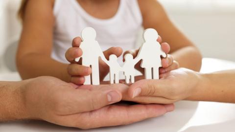 A stock image of adult and children's hands holding a white wooden cutout of a family