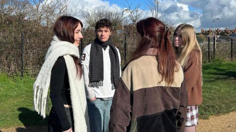 A group of young people standing in a circle in a park talking to each oher