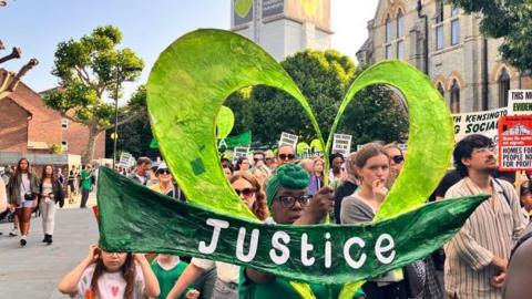 Grenfell campaigners carrying placards and signs march through west London