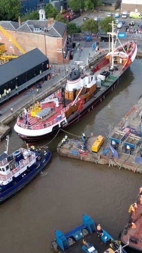 A trawler entering a dock surrounded by pilot boats.
