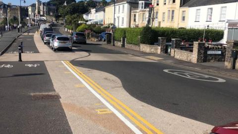 Double yellow lines and parking on seafront with houses and businesses in the background