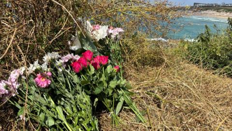 Pink and white flowers left on a cliff overlooking Fistral Beach in Cornwall.