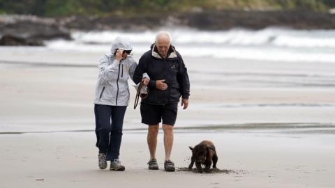 A picture of a couple walking on a Cornwall beach with their dog during Storm Antoni in 2023.