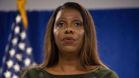 Letitia James stands to deliver a speech with a blue wall behind her and an American flag