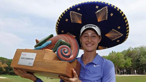 Nelly Korda celebrates winning the Riviera Maya Open in Mexico, wearing a traditional large Mexican hat and blue golf shirt, smiling, and holding a colourful trophy
